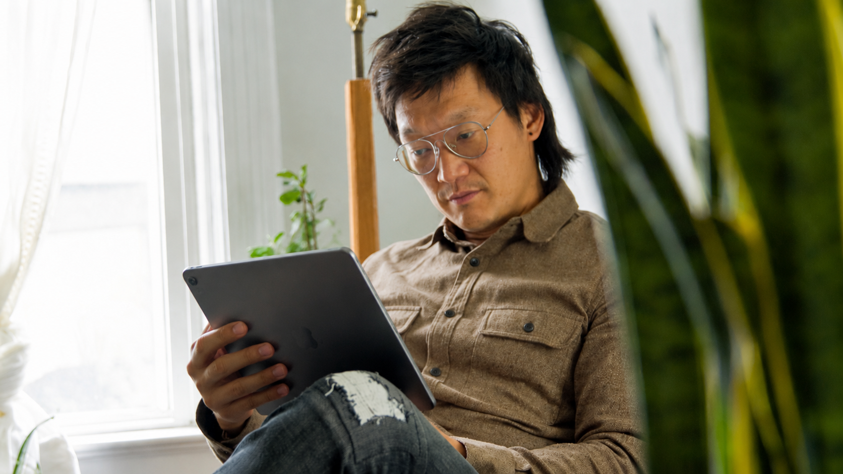 A person reading on a tablet by a sunlit window